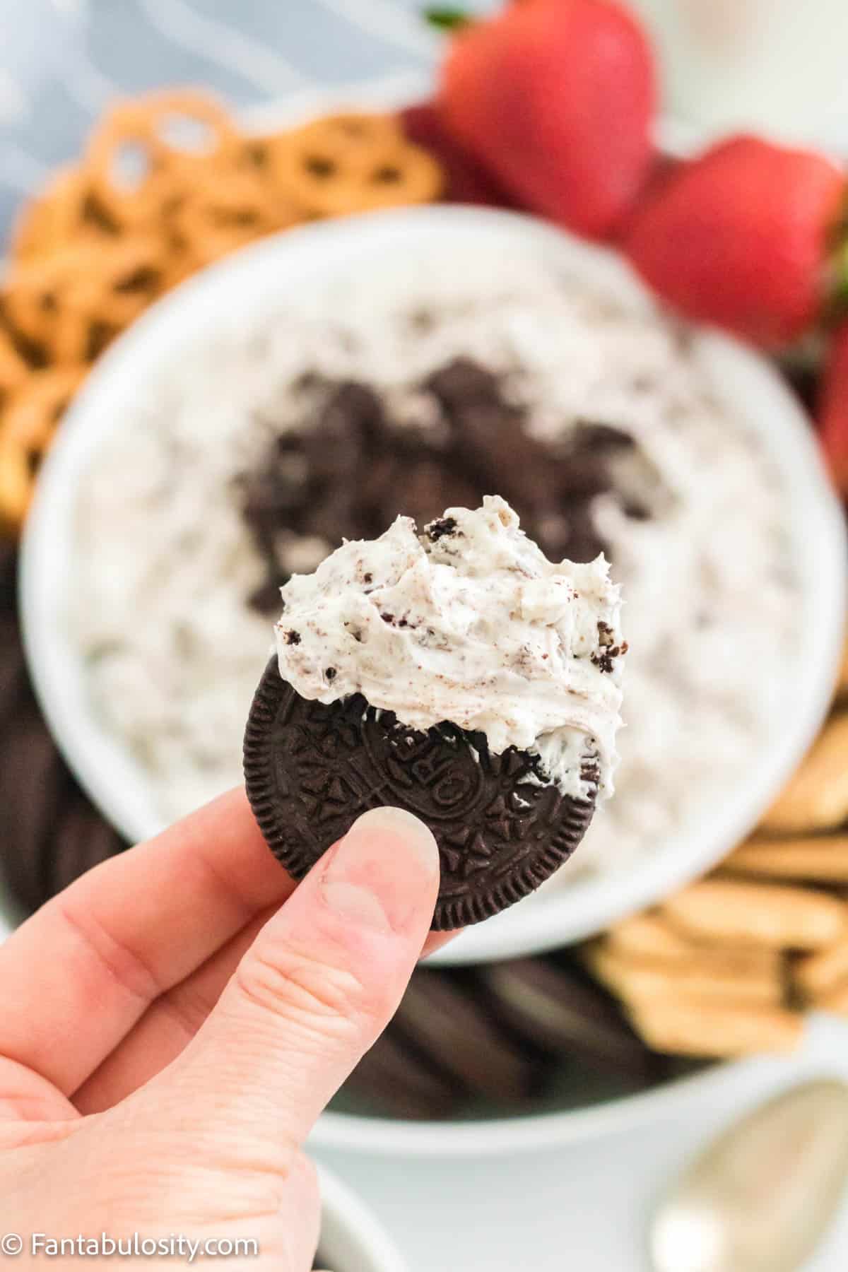 Someone holding an Oreo dipped in Oreo dip.