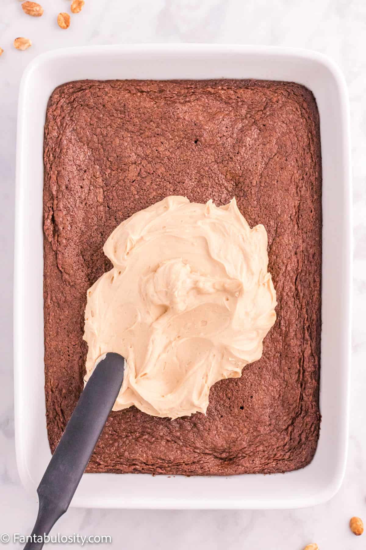 Peanut butter frosting being spread on baked brownies.