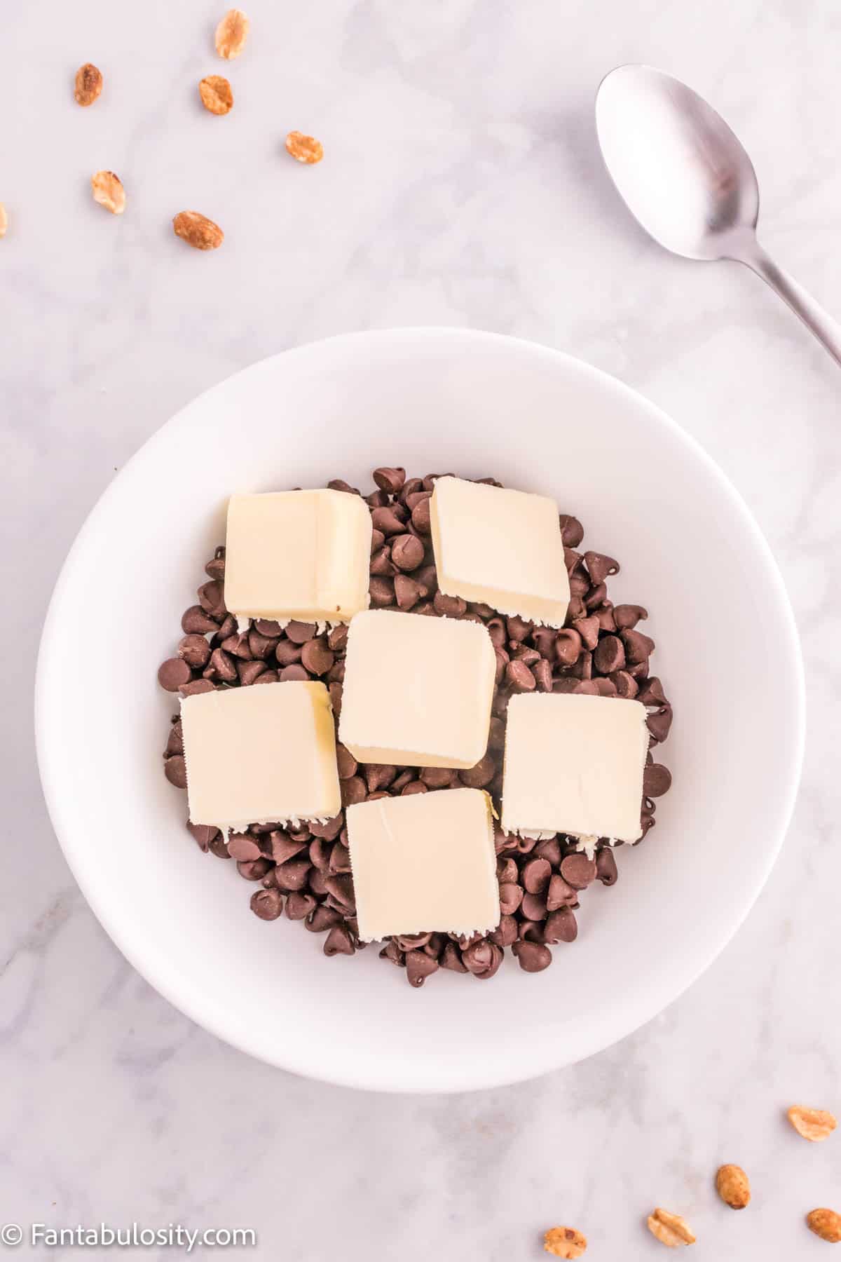 A bowl of chocolate chips with squares of butter all over it.