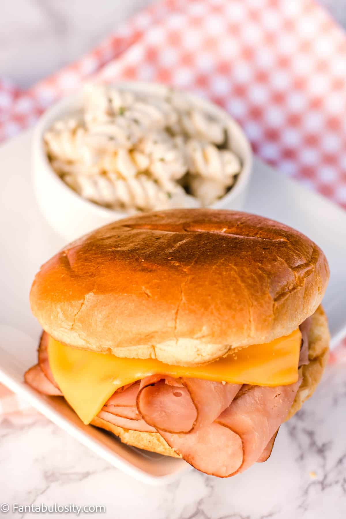 Hot ham and cheese sandwich on white plate next to pasta salad