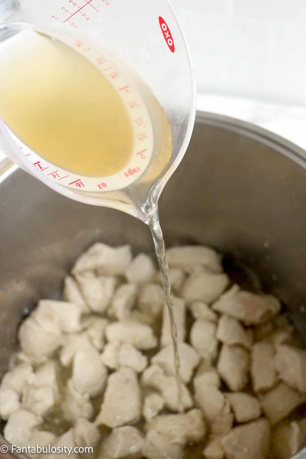 Pouring chicken broth into the Instant Pot with cooked chicken breast pieces in it.