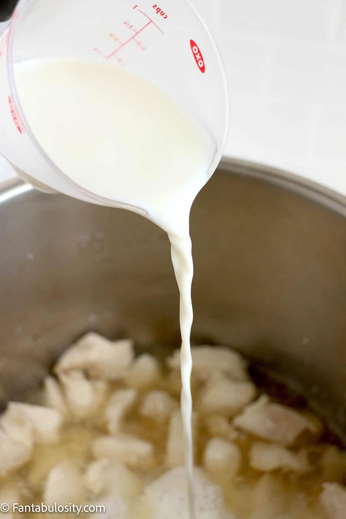 Pouring milk into the Instant Pot with cooked chicken breast pieces in it.