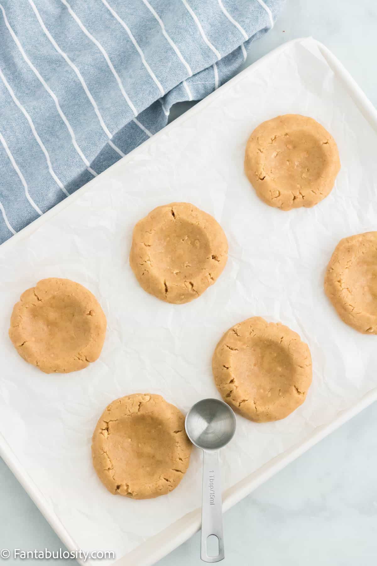 Key lime pie cookie dough balls on a cookie sheet, slightly flattened to create a shallow bowl in each cookie dough. 