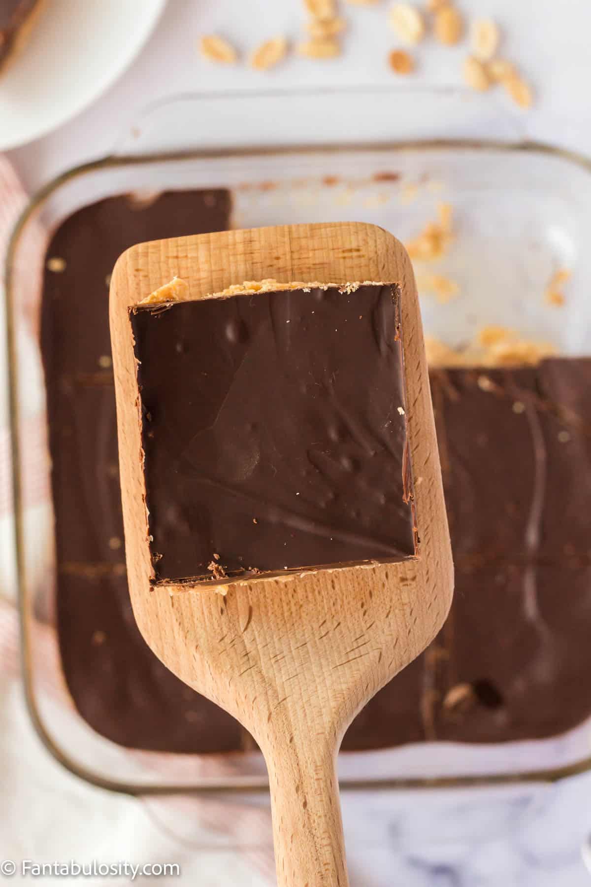 A chocolate peanut butter square on a spatula being held above the 8x8 pan of squares.