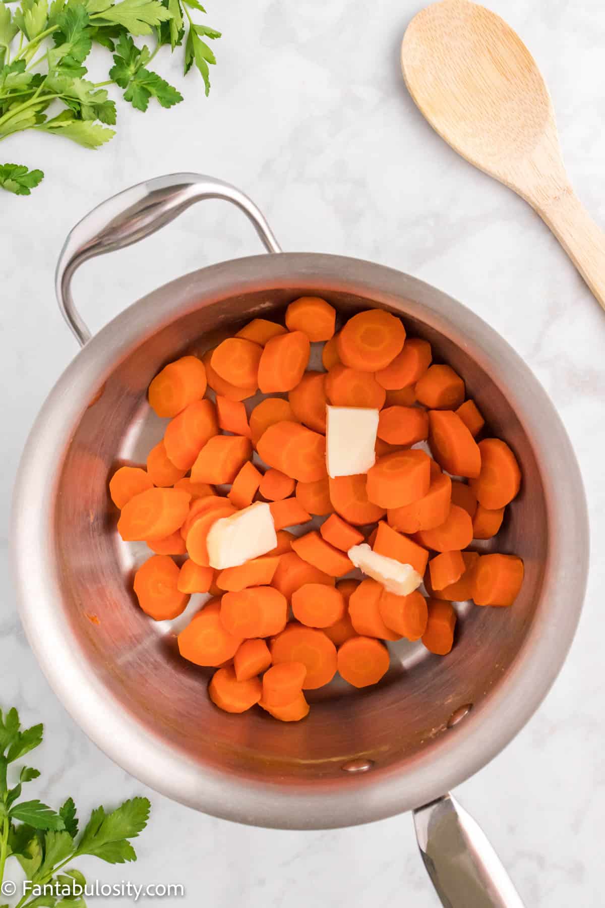 Cooked carrots and several pats of butter are shown in a medium sized saucepan ready to heat to make Candied Carrots