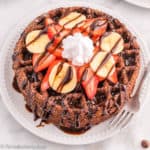 Chocolate Belgian Waffles on a plate topped with fruit, chocolate syrup and whipped cream