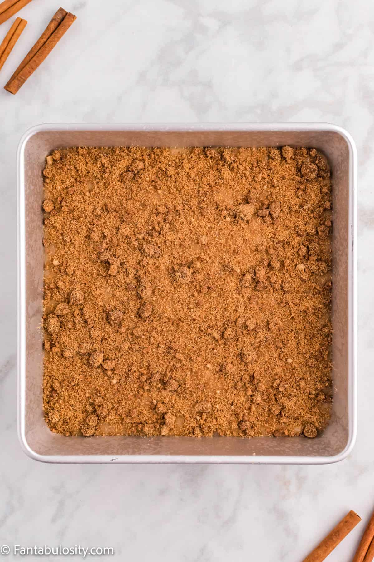 A cake pan is in the center of the photo displaying the cinnamon streusel topping on the top of a Cinnamon Coffee Cake