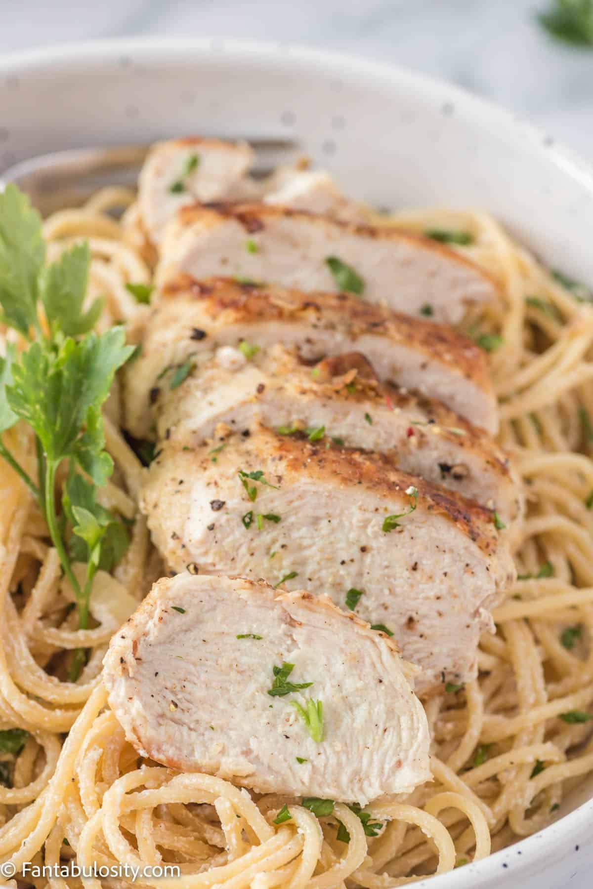 Close up of cooked spaghetti noodles coated with creamy lemon Parmesan sauce and topped with a sliced chicken breast and fresh parsley