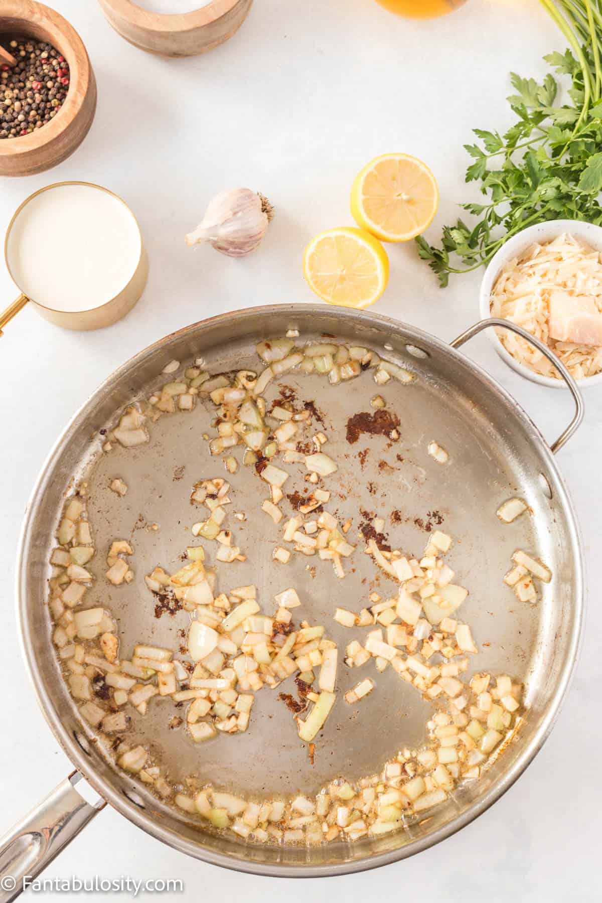 A pan is centered with onions and garlic sauteeing in olive oil for Creamy Lemon Chicken Pasta
