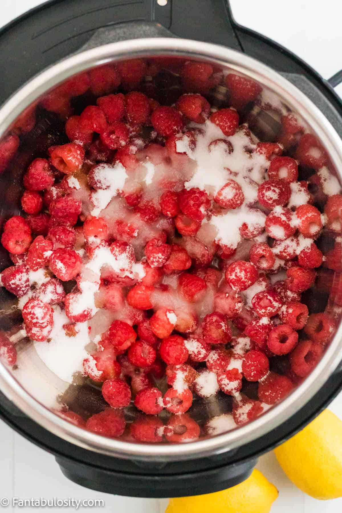 The inside of an Instant Pot pressure cooker is filled with fresh raspberries, sugar and lemon juice ready to make Instant Pot raspberry jam