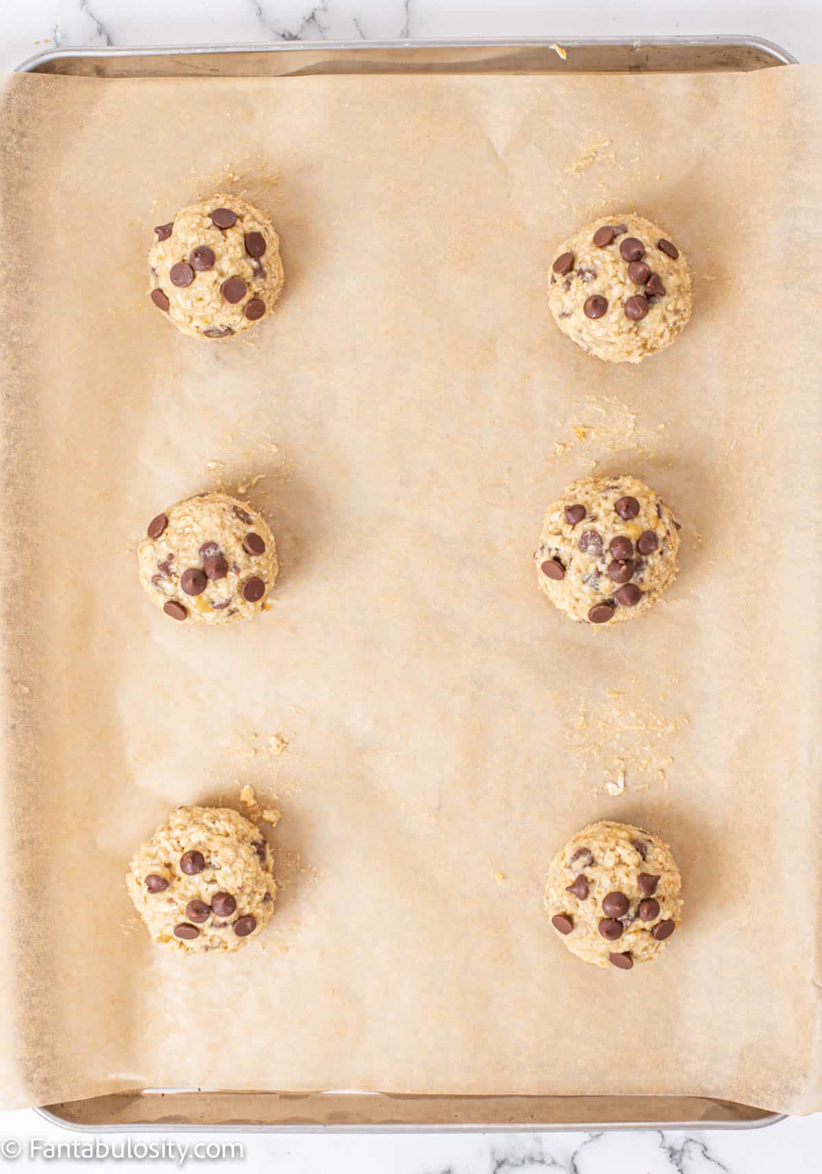 Balls of banana chocolate chip cookie dough on a parchment lined baking sheet.