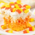 Close up photo of a frosted tri-colored piece of cake with candy corn on it