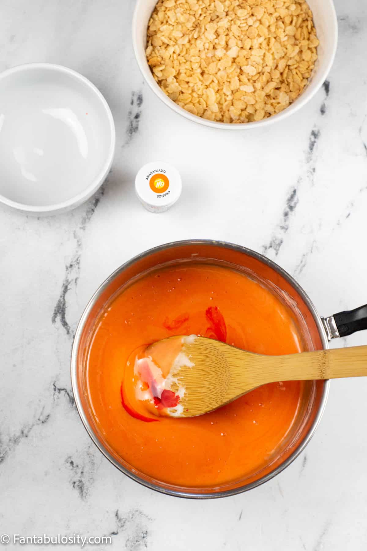 Orange food coloring is stirred into a pan that contains melted butter and marshmallows for a layer of candy corn rice krispie treats