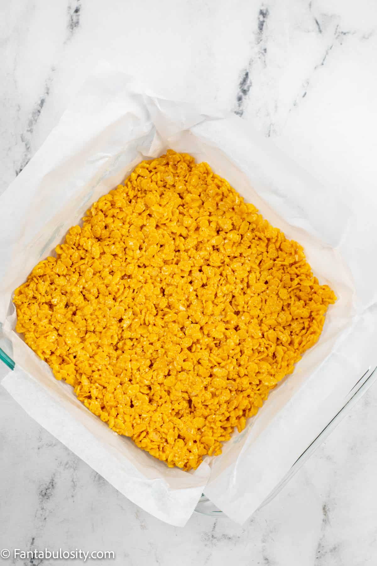 An 8x8 cake pan is filled with a layer of yellow rice kripie treats for candy corn rice krispie treats