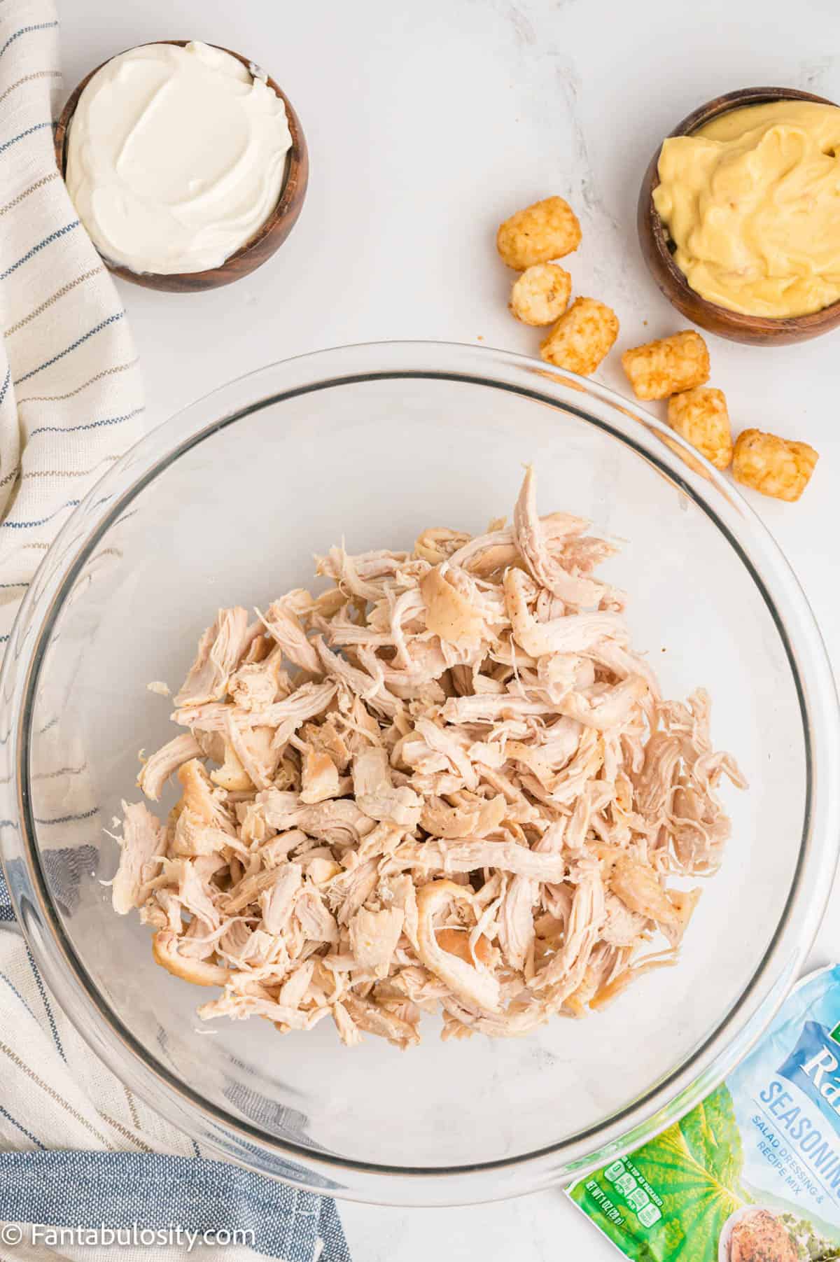 Cooked shredded chicken is in a large glass mixing bowl
