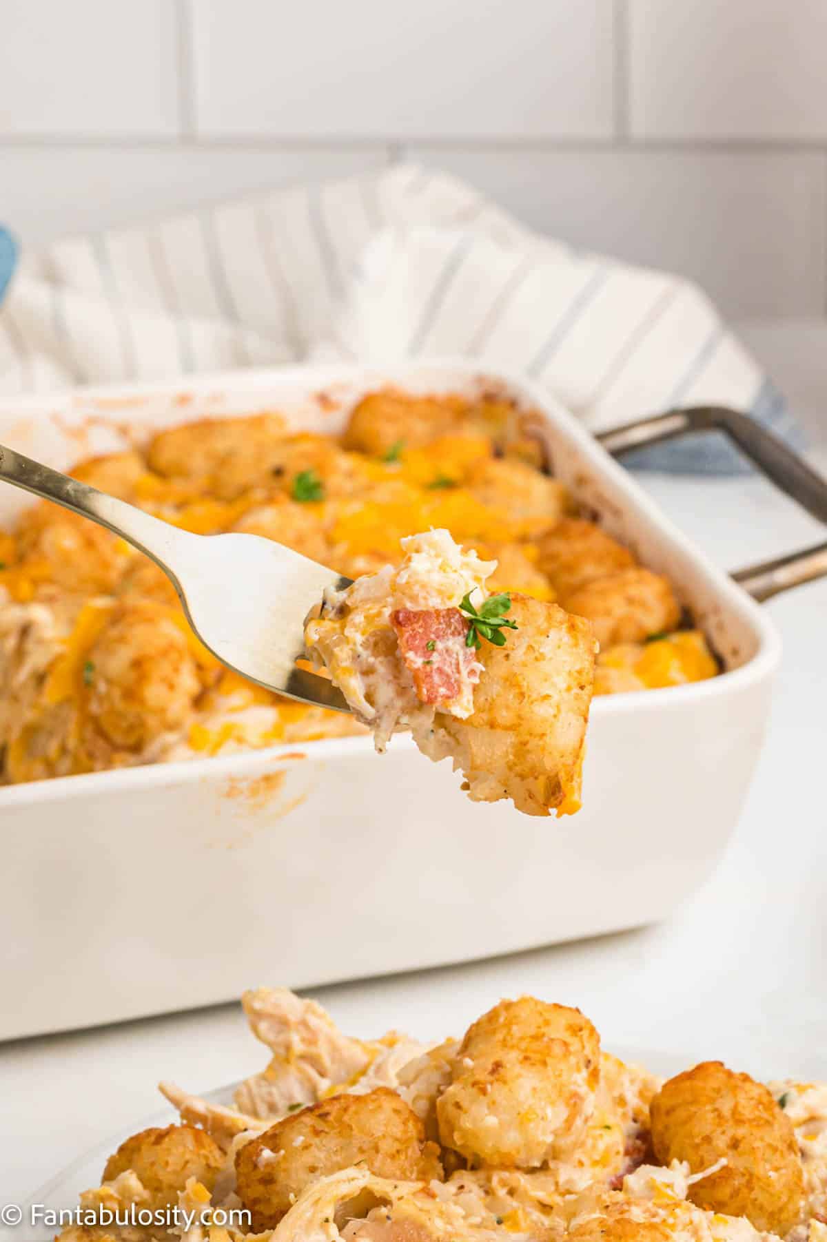 A fork holds a bite of creamy cheesy chicken casserole above a plate portion of the same meal
