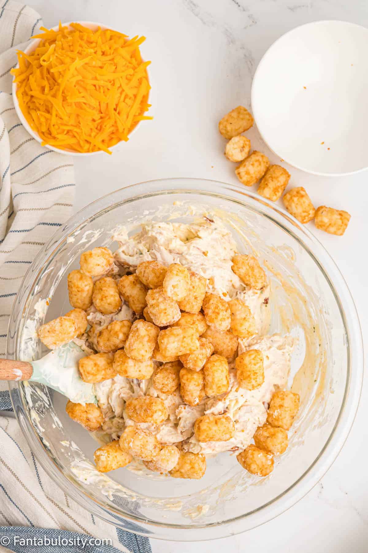 Frozen tater tots have been added to a glass mixing bowl with a creamy chicken mixture