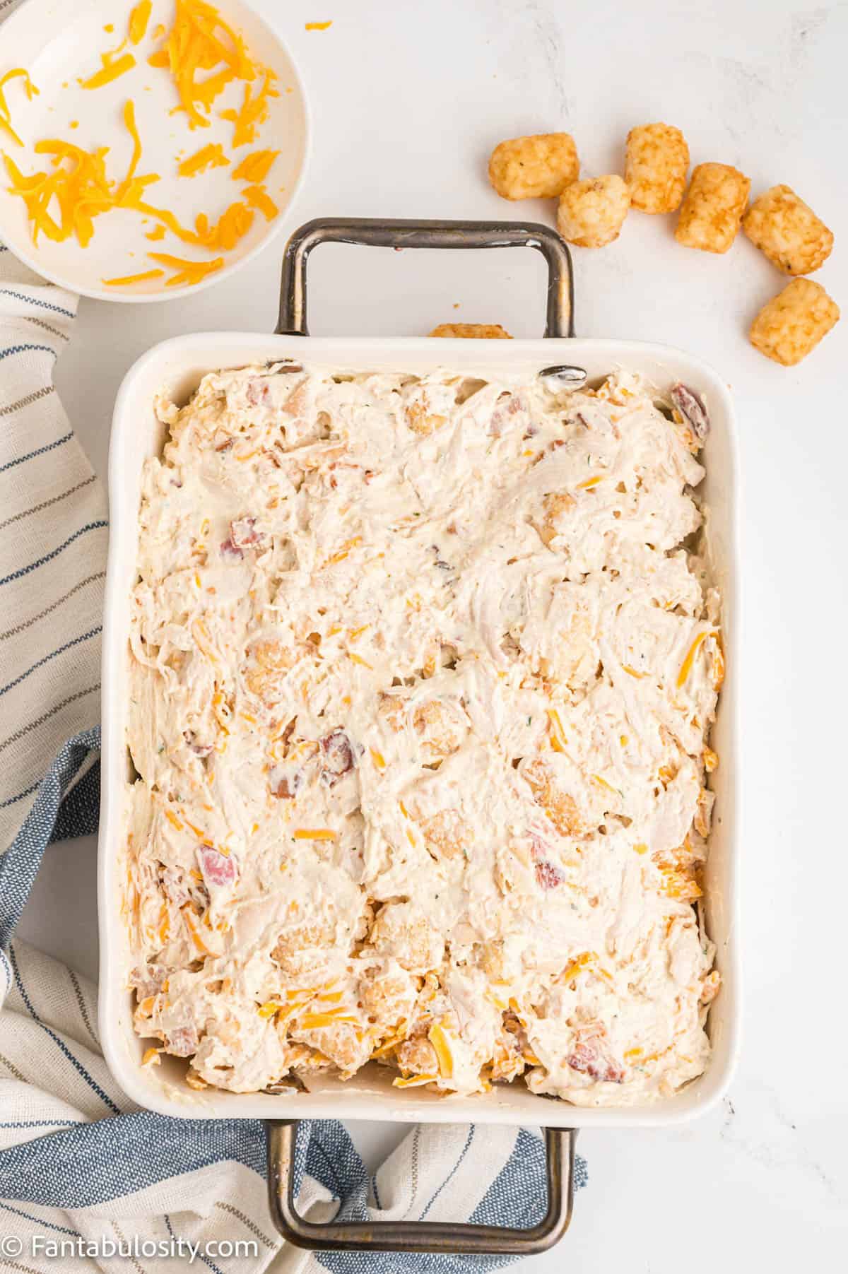 A white baking dish holds the unbaked contents of a creamy cheesy casserole ready to be baked