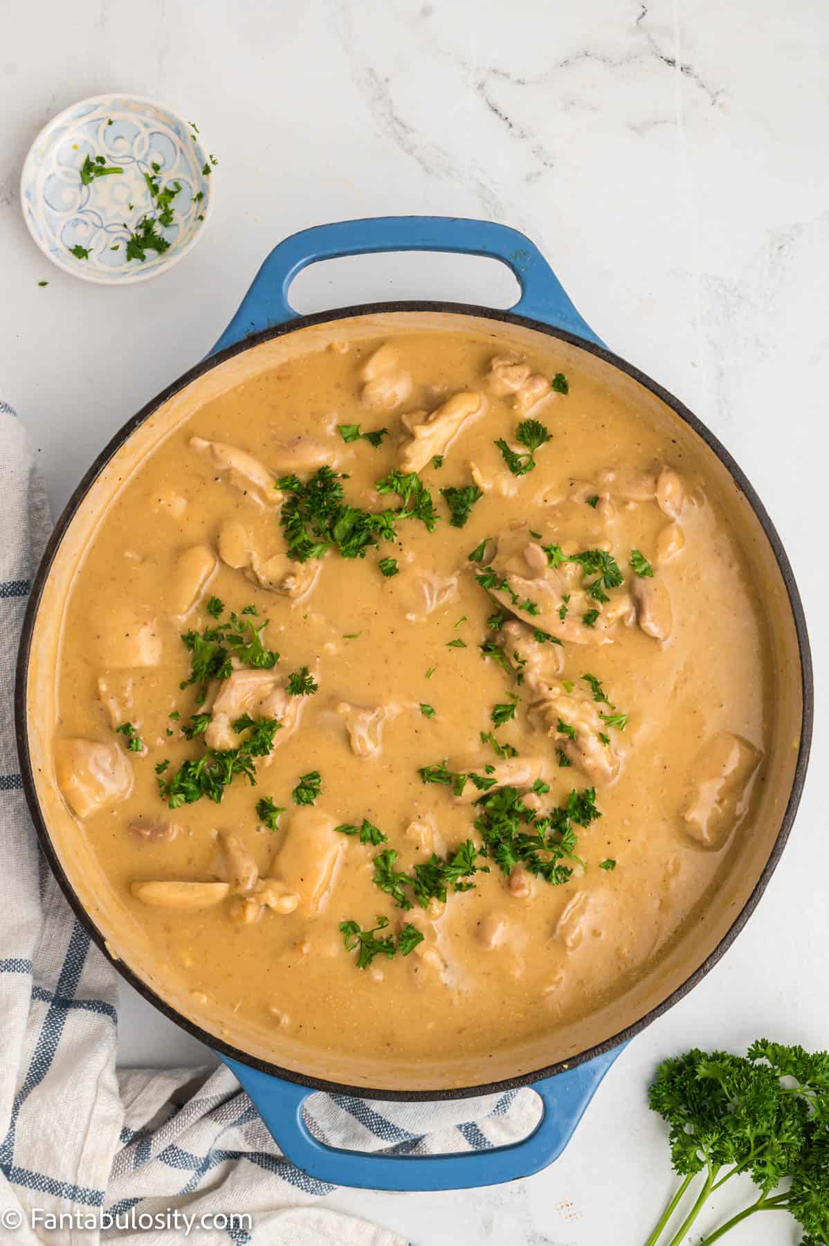 Vibrant green fresh parsley has been sprinkled over a large pan of creamy chicken and gravy