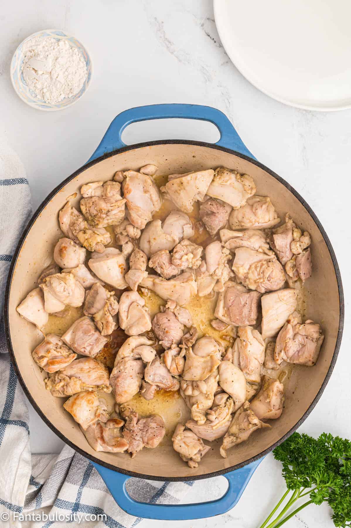Bite sized pieces of seasoned cooked chicken are shown in a large pan