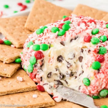 Close up of a plated dessert cheese ball covered in crushed candy canes and mini M&Ms that is surrounded by graham crackers