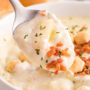 A close up photo of a spoon of clam chowder with bacon bits and parsley