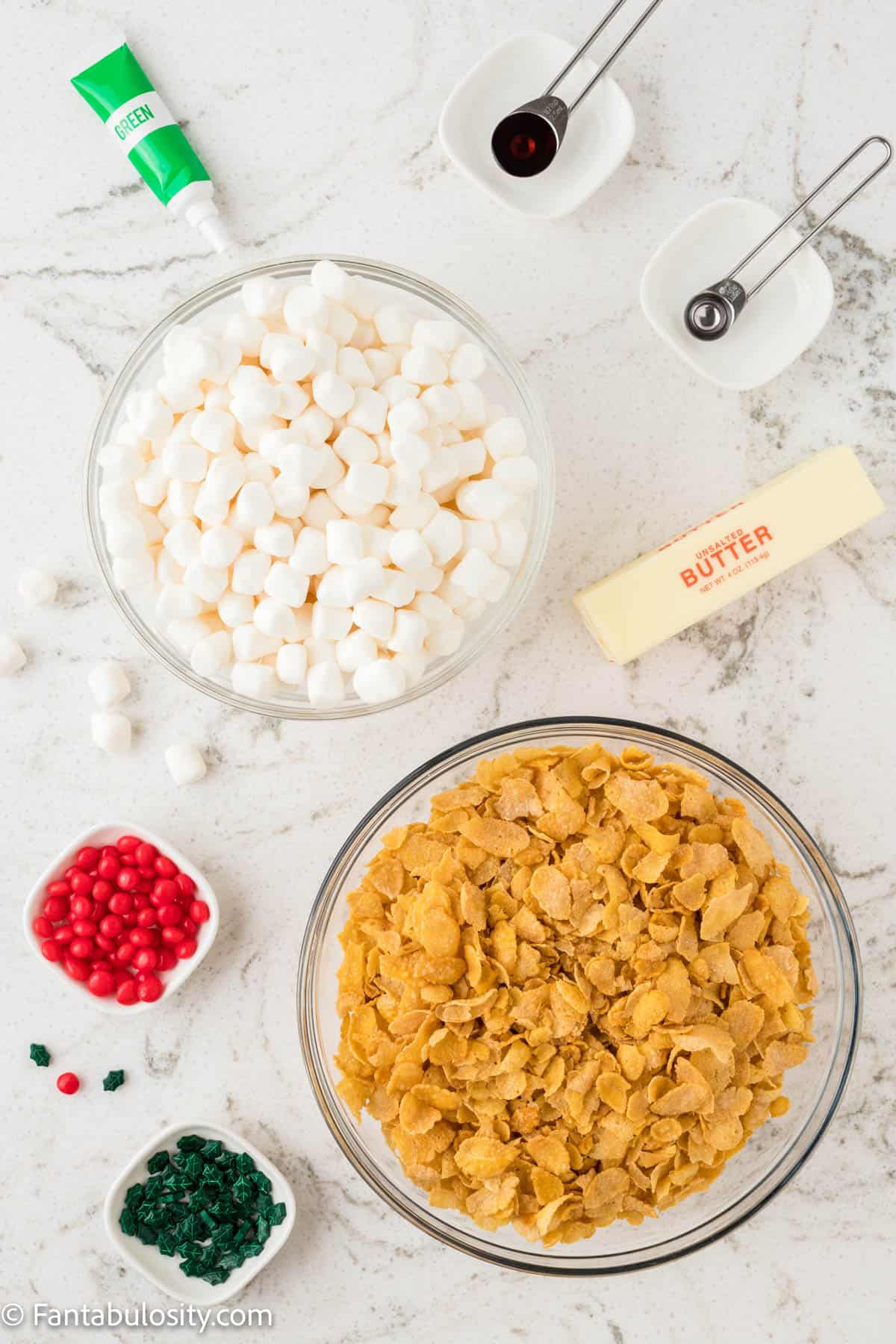 The ingredients to make cornflake wreath cookies are displayed in bowls on a white marble countertop