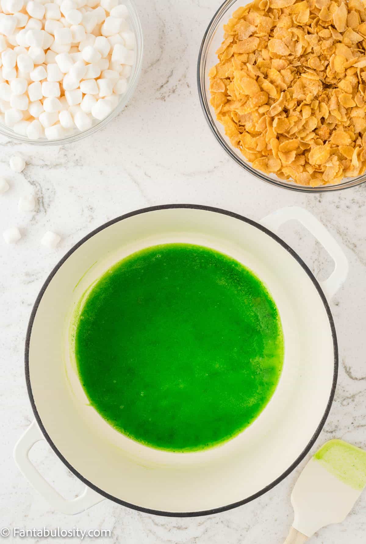 Green food coloring has been added to melted butter in a large pot in preparation to make cornflake wreath cookies