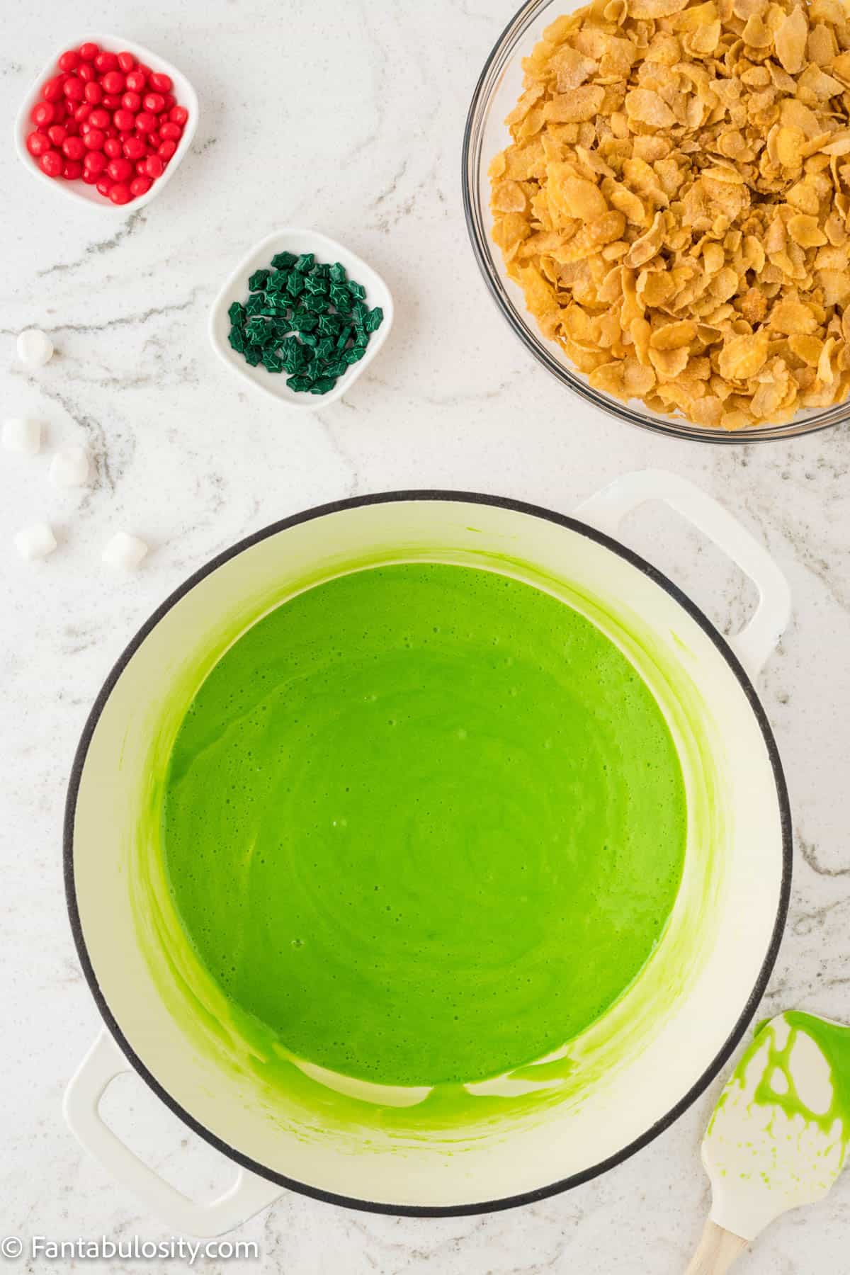 Mini marshmallows, melted butter and green food coloring have been melted and stirred together in a large pot in the center of the photo