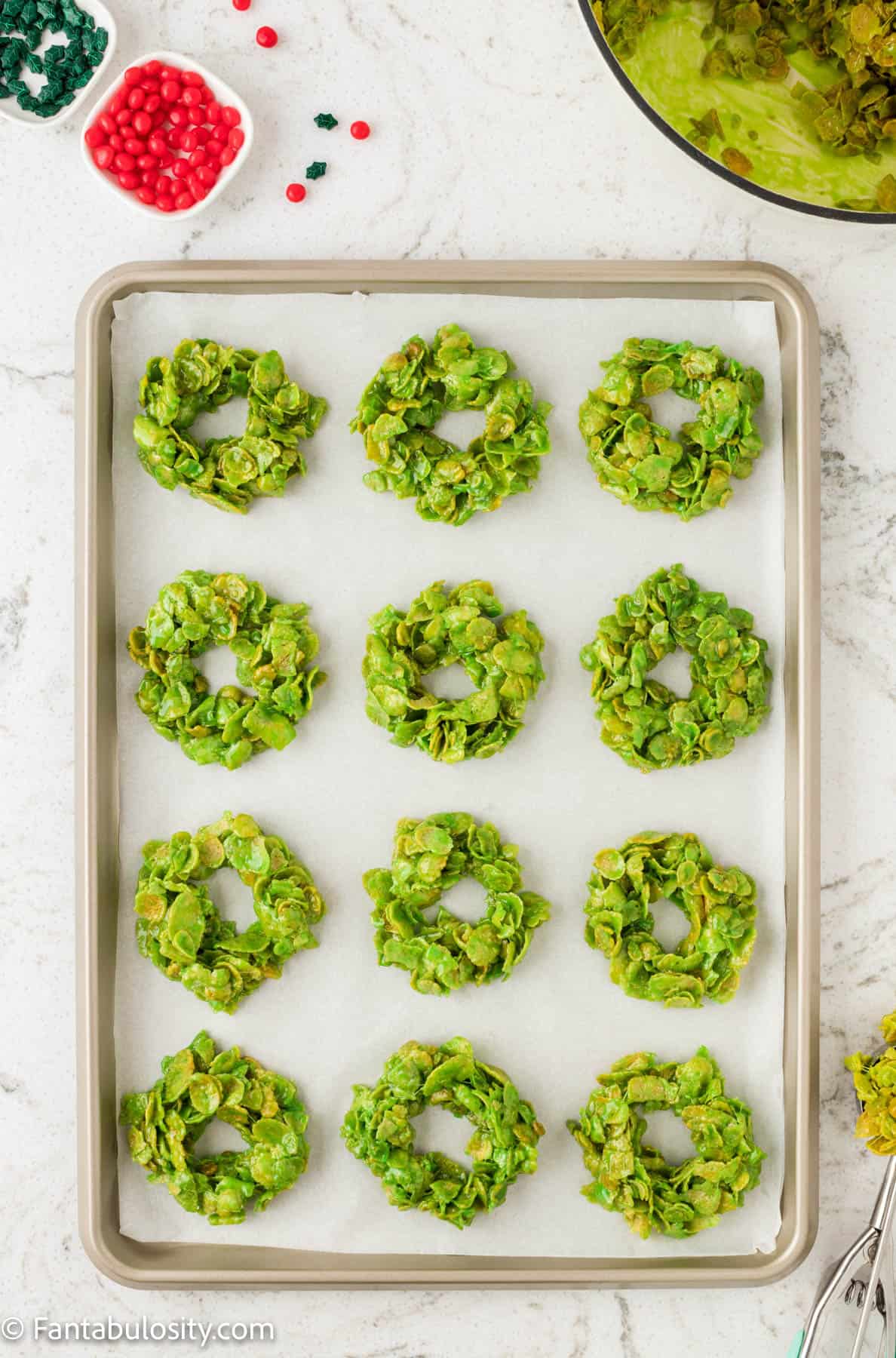 Green marshmallow coated cornflakes have been shaped into wreath shapes on a parchment lined baking sheet