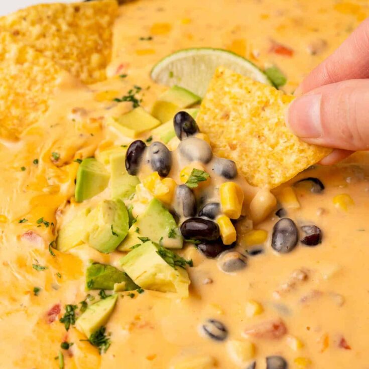 A tortilla chip is being dipped into a big bowl of cowboy queso.