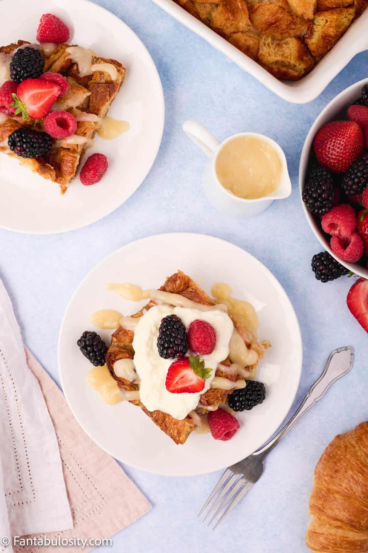 Plates of bread pudding garnished with fresh berries, a small pitcher of vanilla sauce, a bowl of berries and forks are included in a welcoming breakfast spread