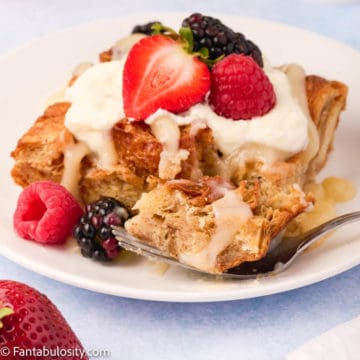 A serving of bread pudding sits on a white plate garnished with fresh berrries and vanilla sauce