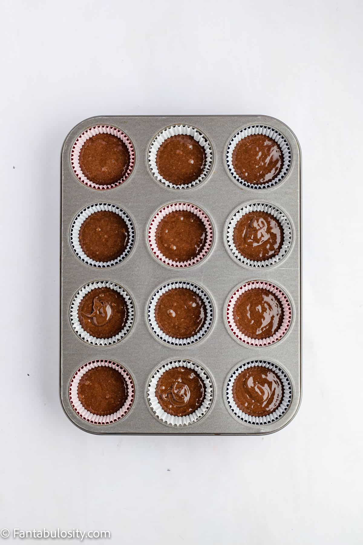 A 12 cup muffin tin is filled with chocolate cupcake batter ready to be baked