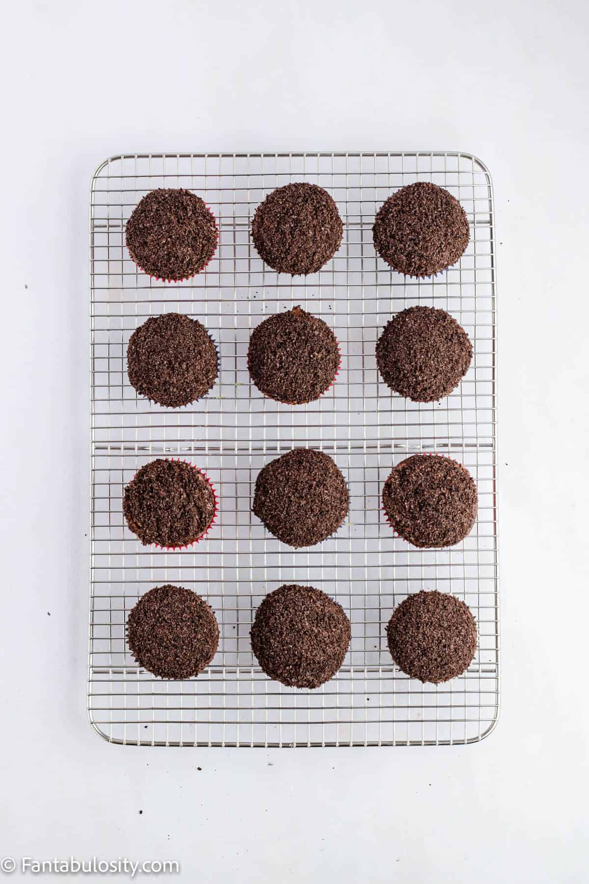 12 chocolate cupcakes with chocolate frosting and Oreo crumbs are displayed on a wire cooling rack