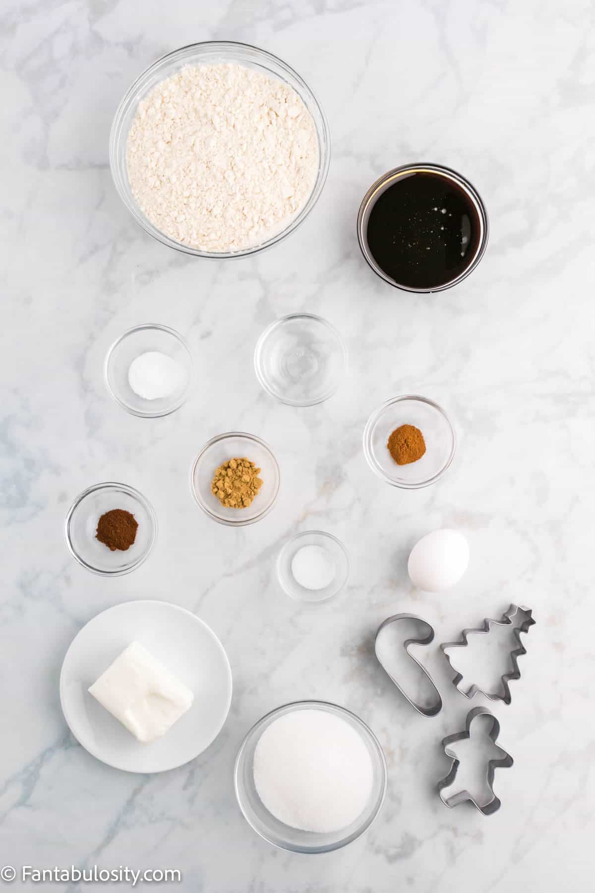 Bowls of ingredients and cookie cutters are displayed on a white marbled background