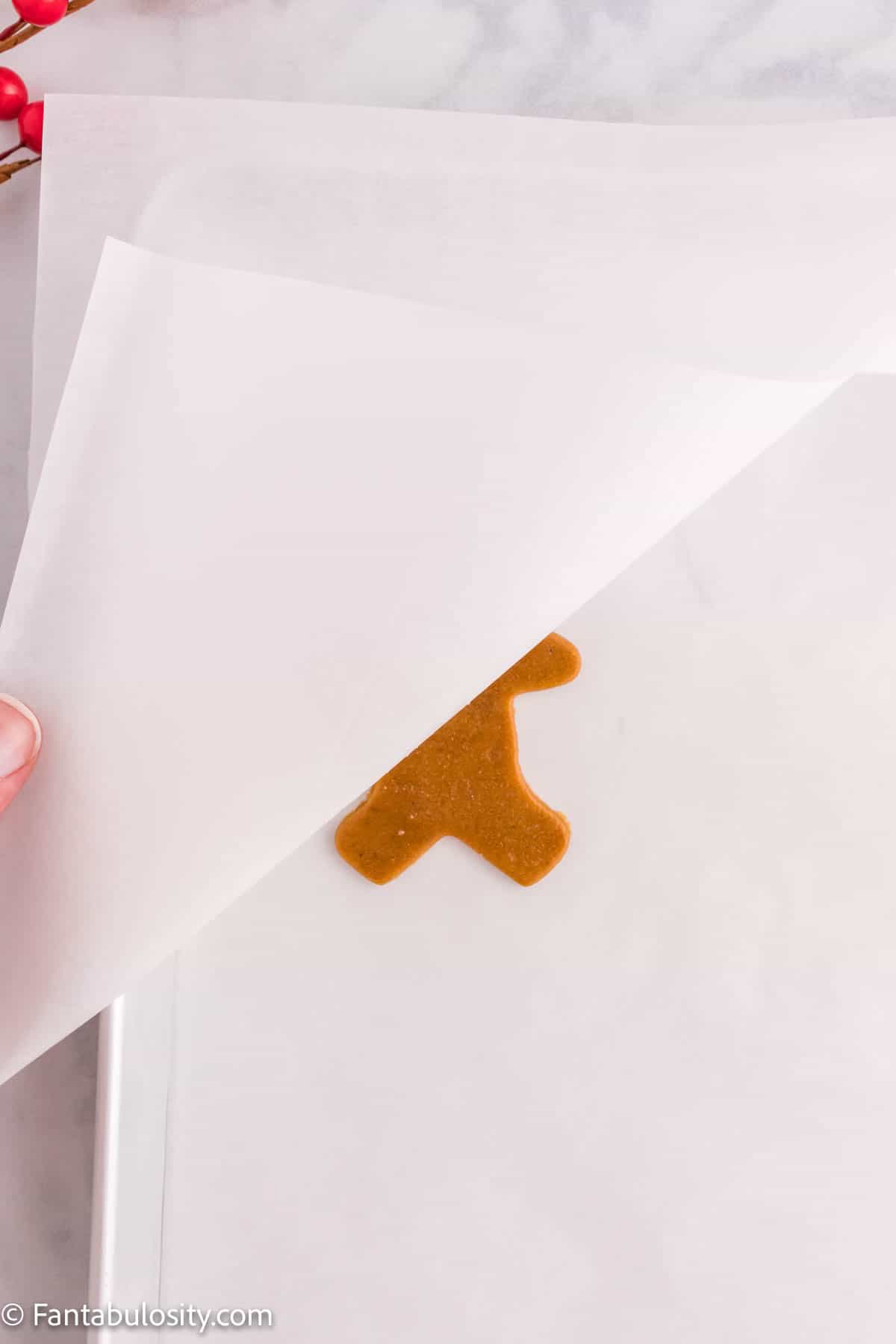 A sheet of parchment paper is being lifted to reveal a cut out christmas cookie underneath