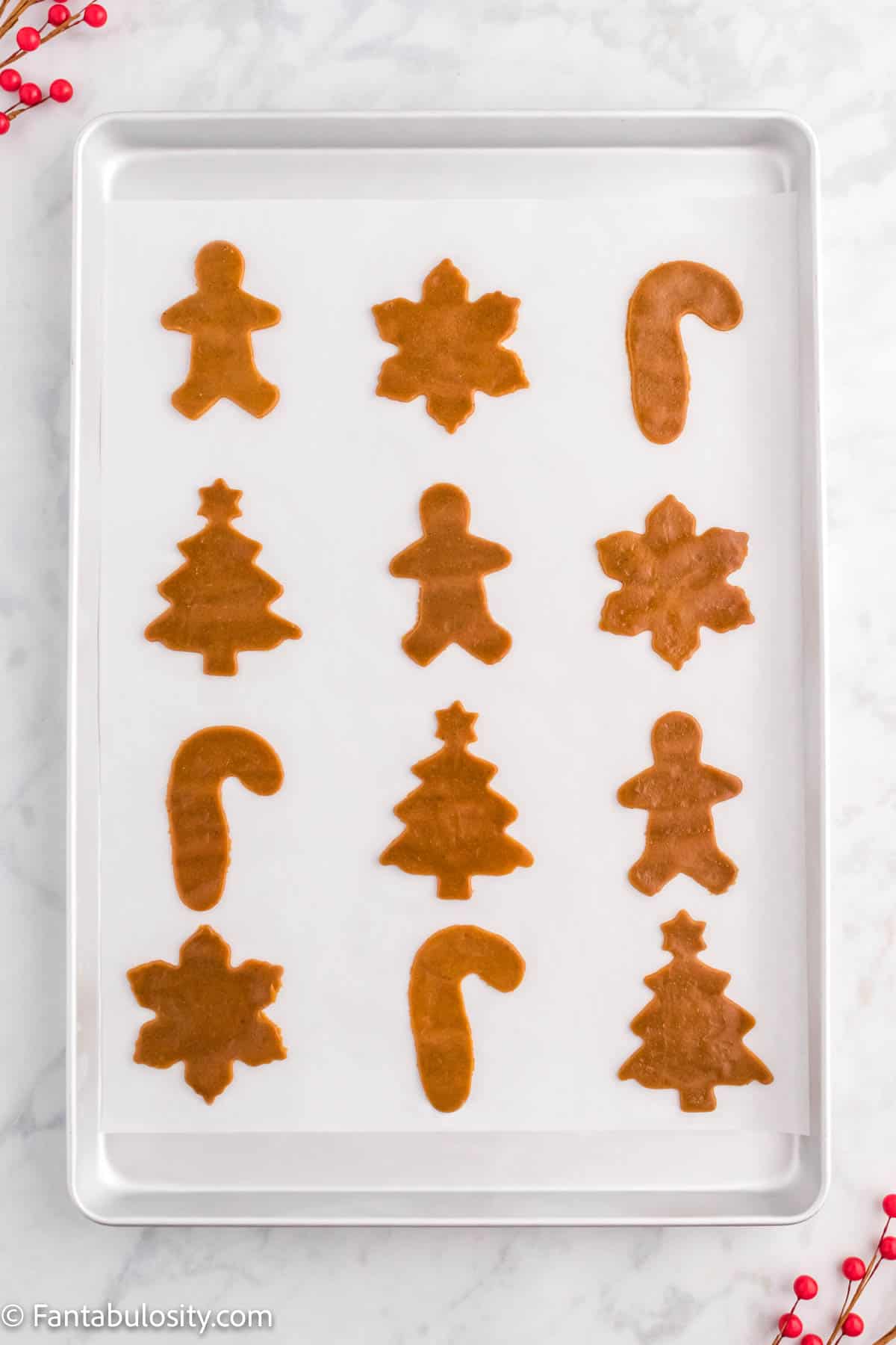 A baking sheet lined with parchment paper holds 12 cut out gingerbread cookies ready to be baked