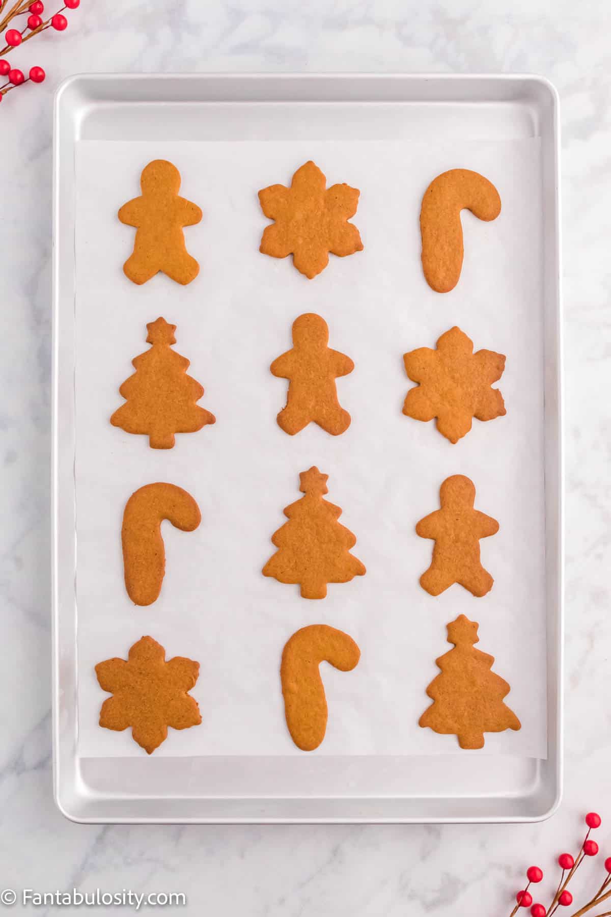 A metal baking sheet lined with parchment paper holds a dozen baked unfrosted gingerbread cookies