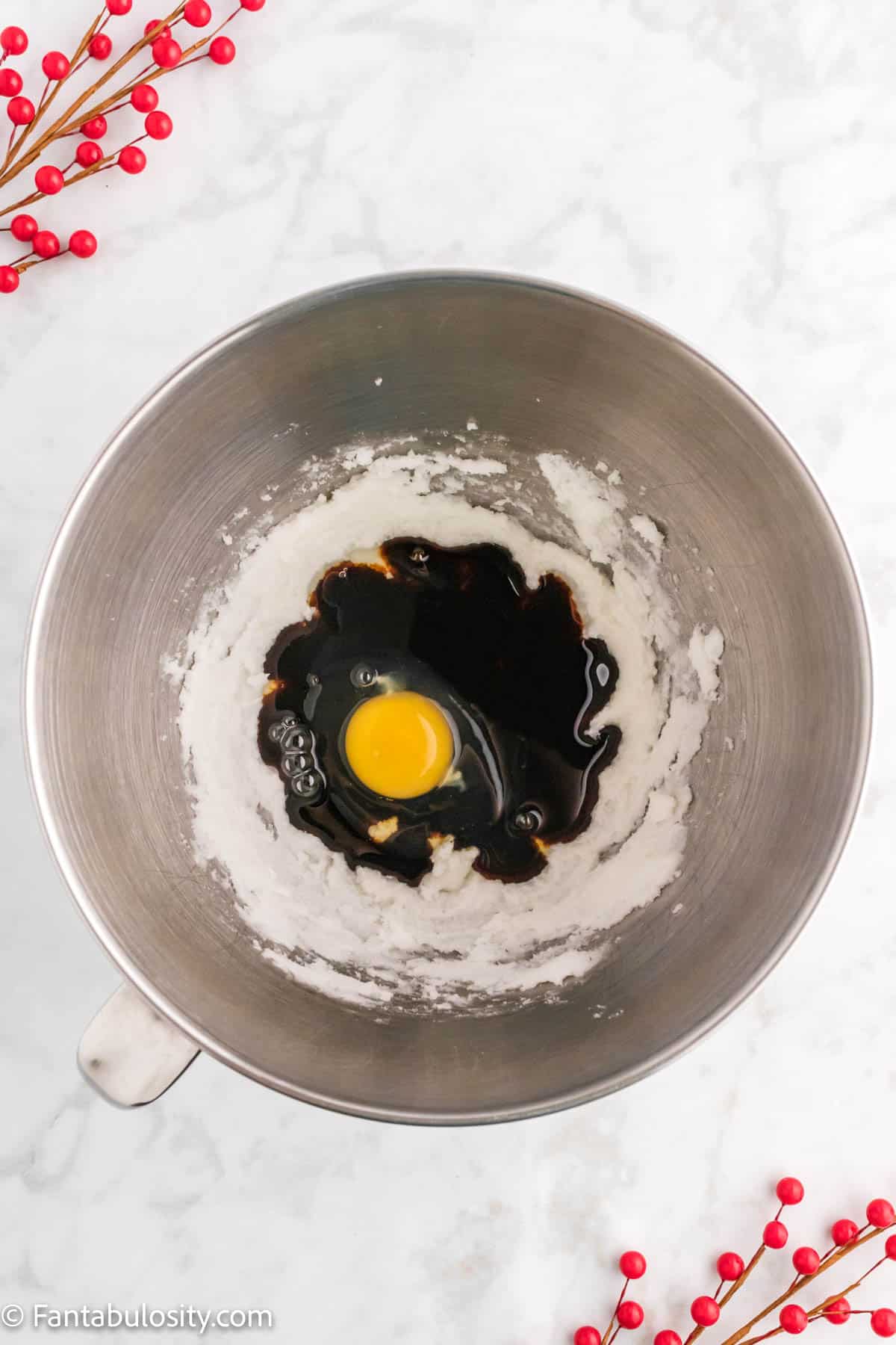 A metal mixing bowl holds a creamed mixture, an egg and molasses ready to be mixed