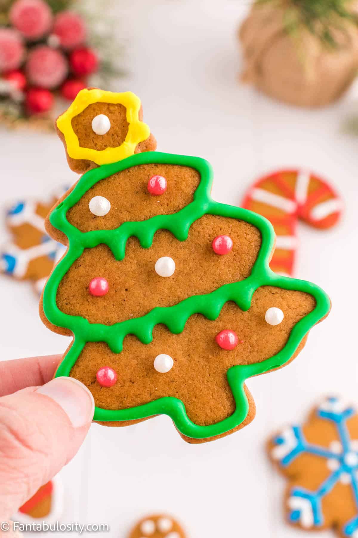 A hand is holding a Christmas tree shaped gingerbread cookie with bright frosting and pearl sugar ornaments