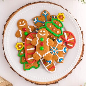 A white plate holds brightly decorated cut out gingerbread cookies in the shapes of gingerbread people, snowflakes, candy canes and Christmas trees