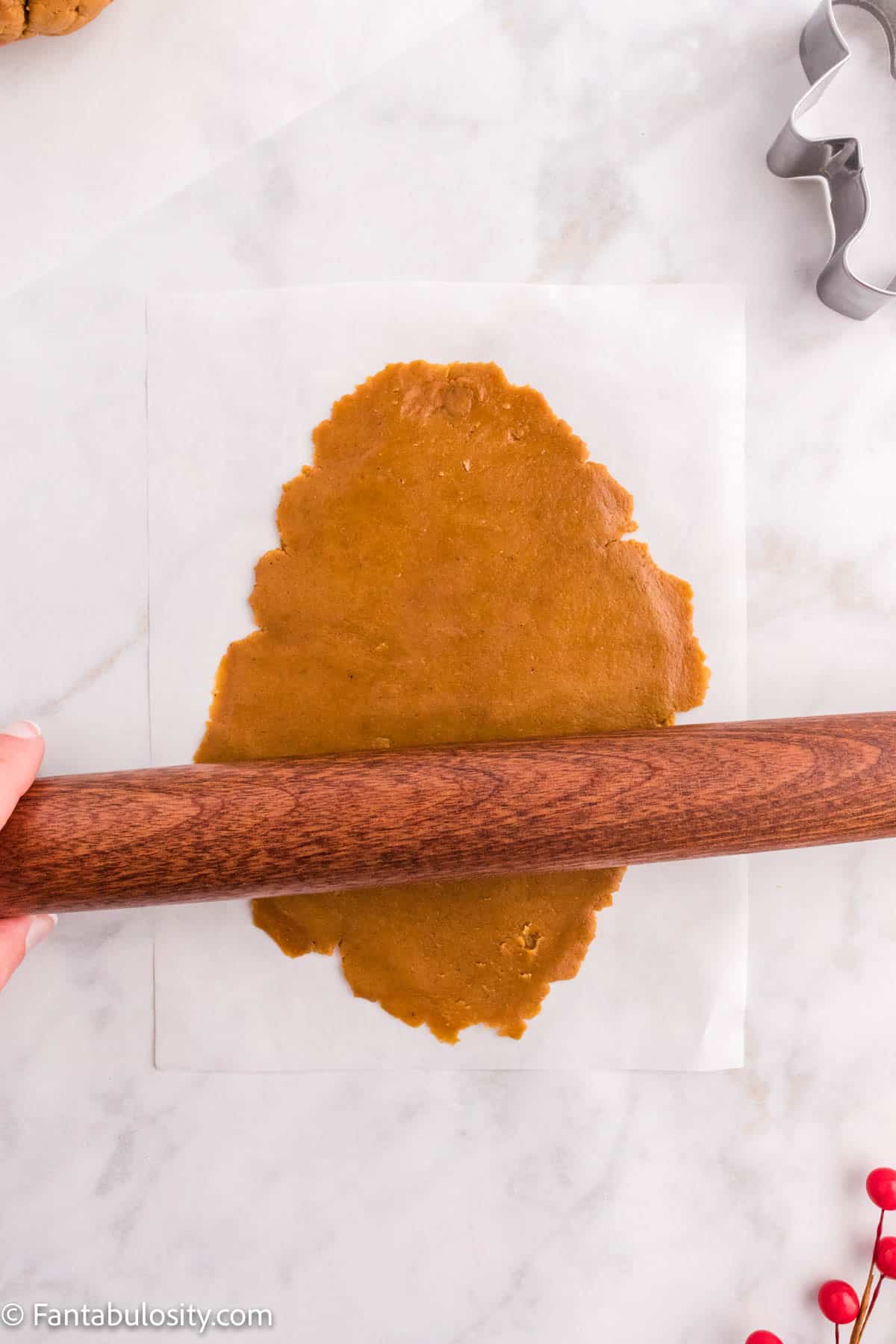 Cookie dough is being rolled out on parchment paper with a wooden rolling pin