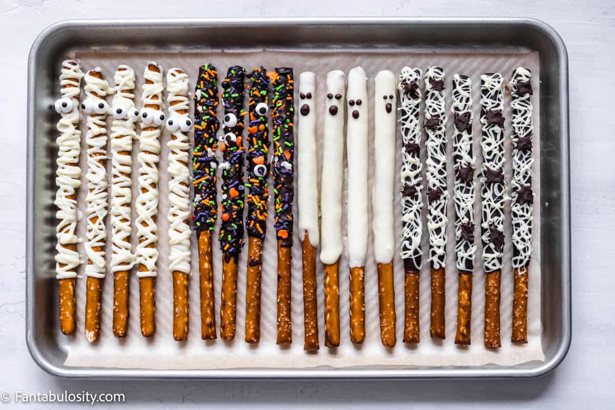 4 types of Halloween chocolate dips pretzel rods are lined up on a parchment lined baking sheet