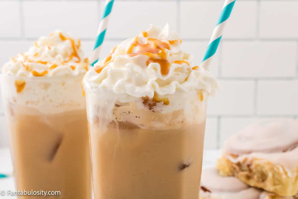 Close up photo of a two glasses of iced caramel latte, topped with whipped cream and caramel with a teal and white striped straw