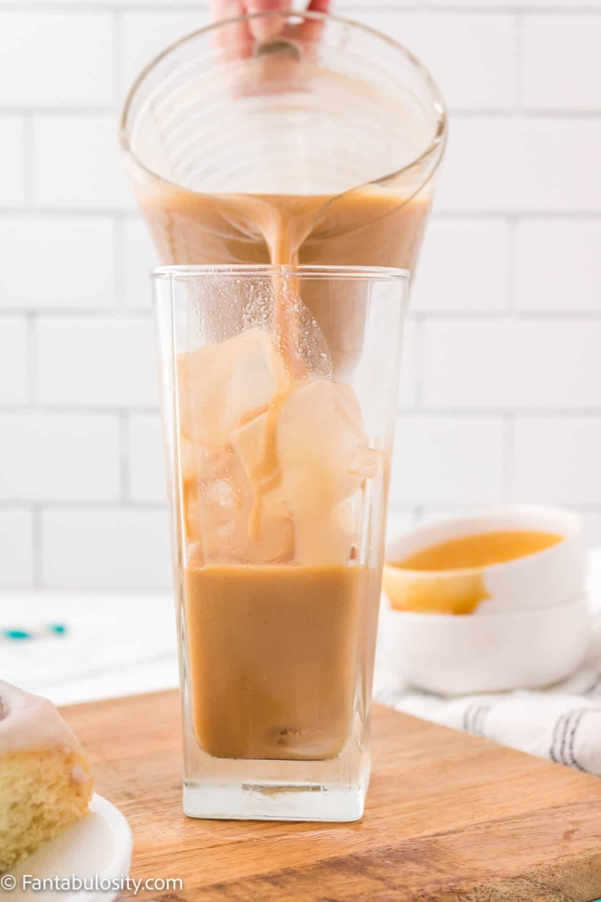 Coffee with caramel and cream is being poured into a tall glass full of ice