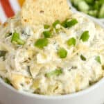 A tortilla chip being dipped in a bowl of jalapeño artichoke dip.