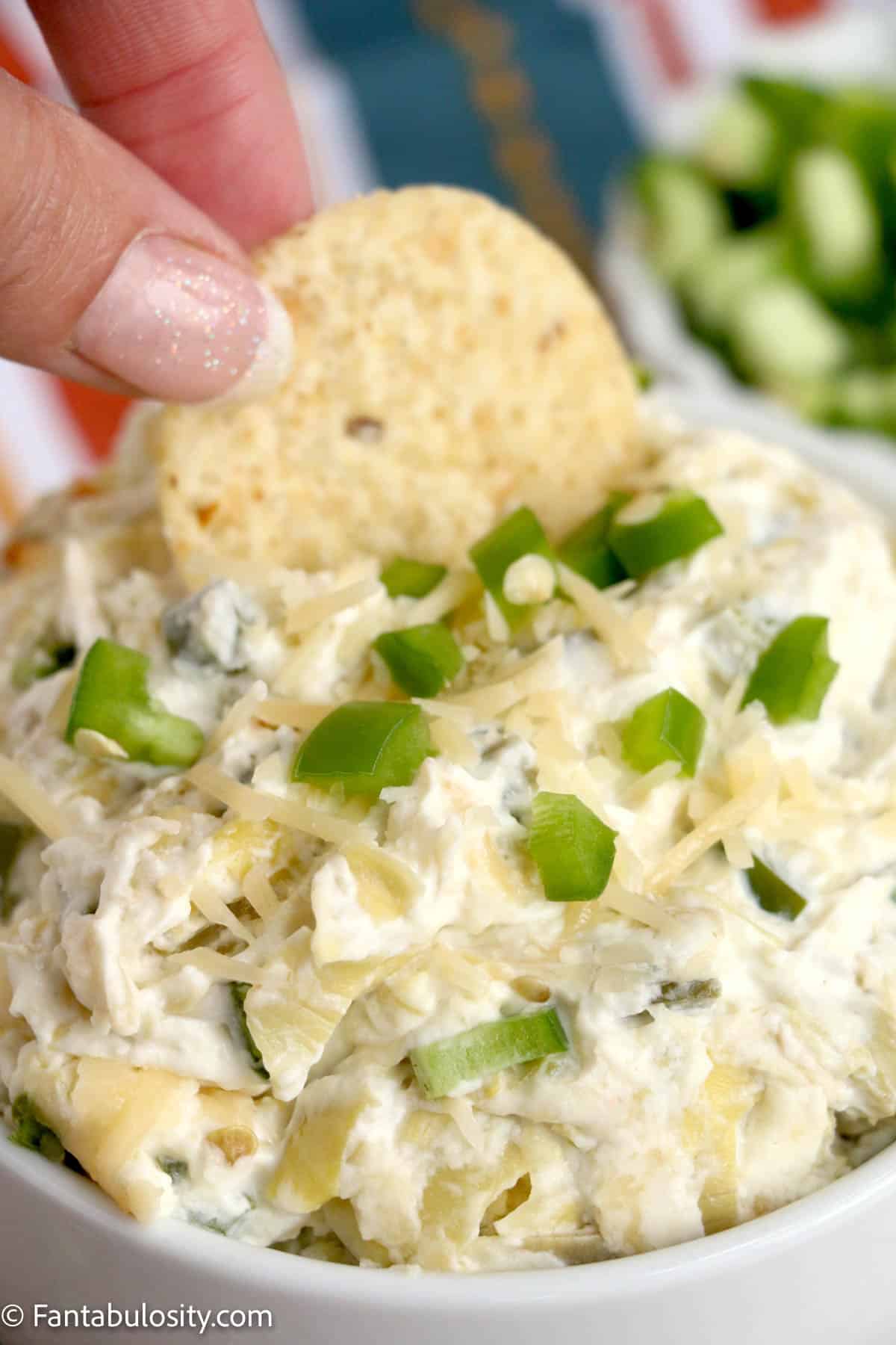 A tortilla chip being dipped in a bowl of jalapeño artichoke dip.