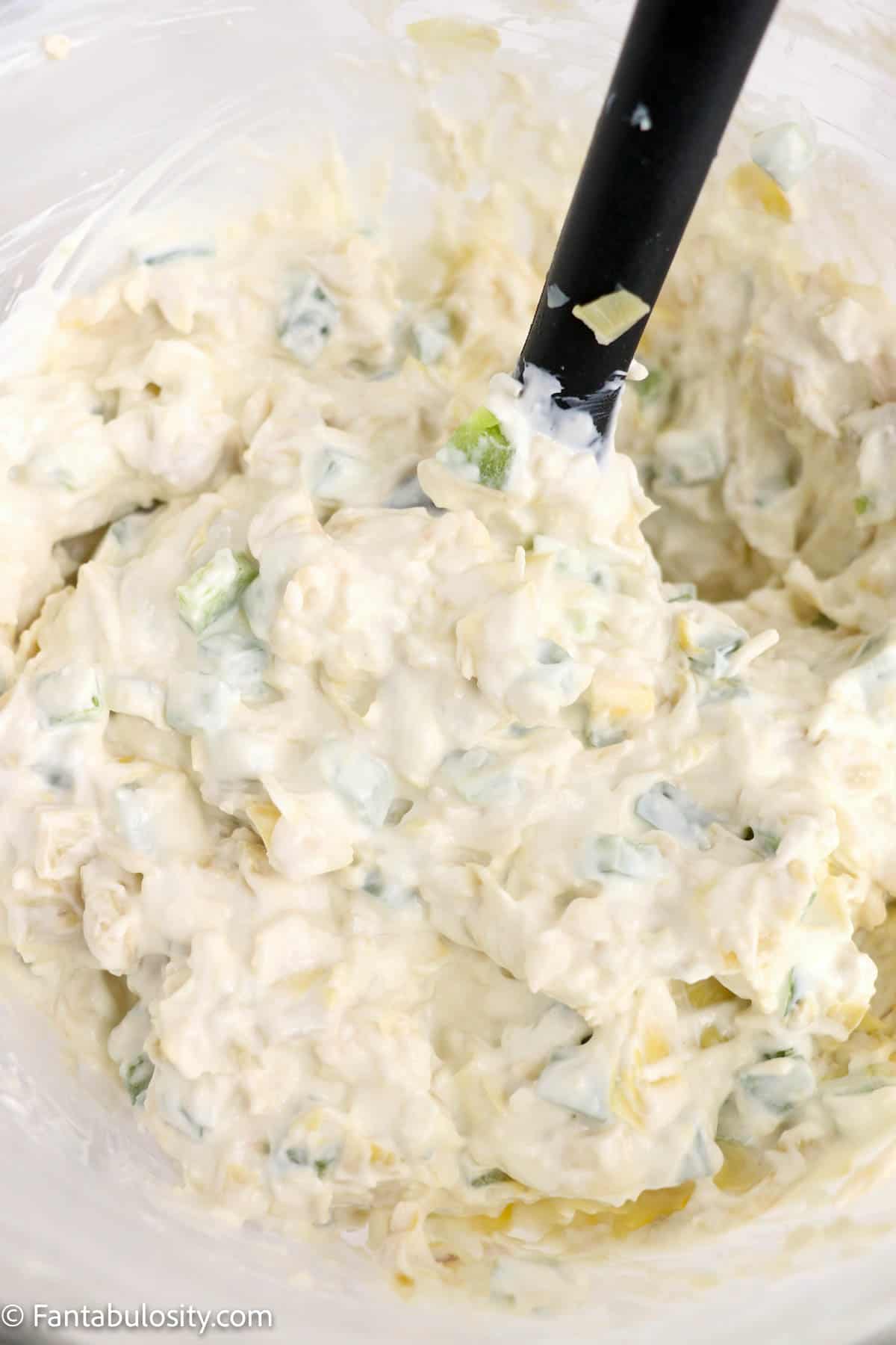 Jalapeno artichoke dip being stirred together in a mixing bowl.