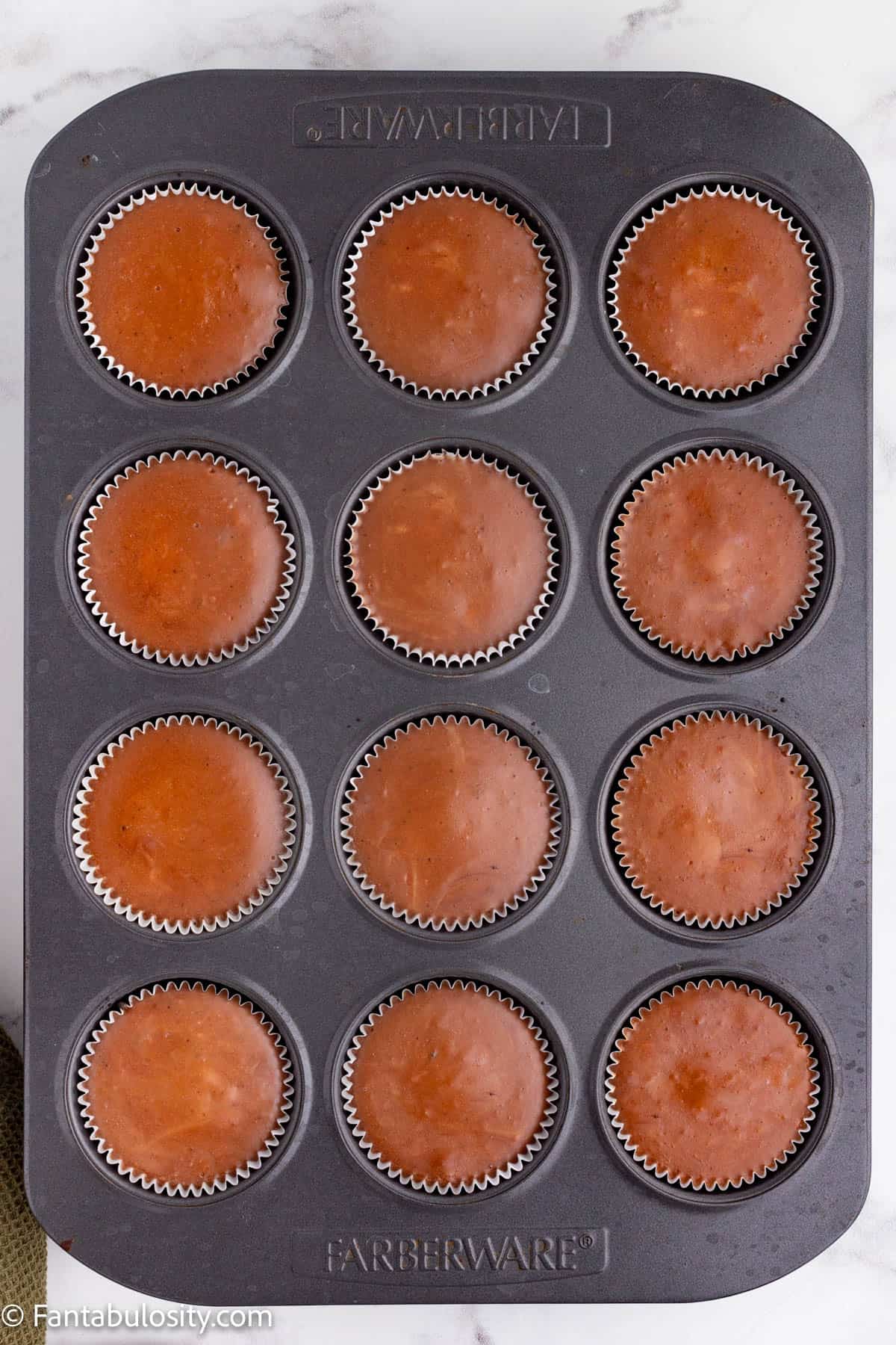 A metal cupcake tin holds 12 baked chocolate cheesecake cups